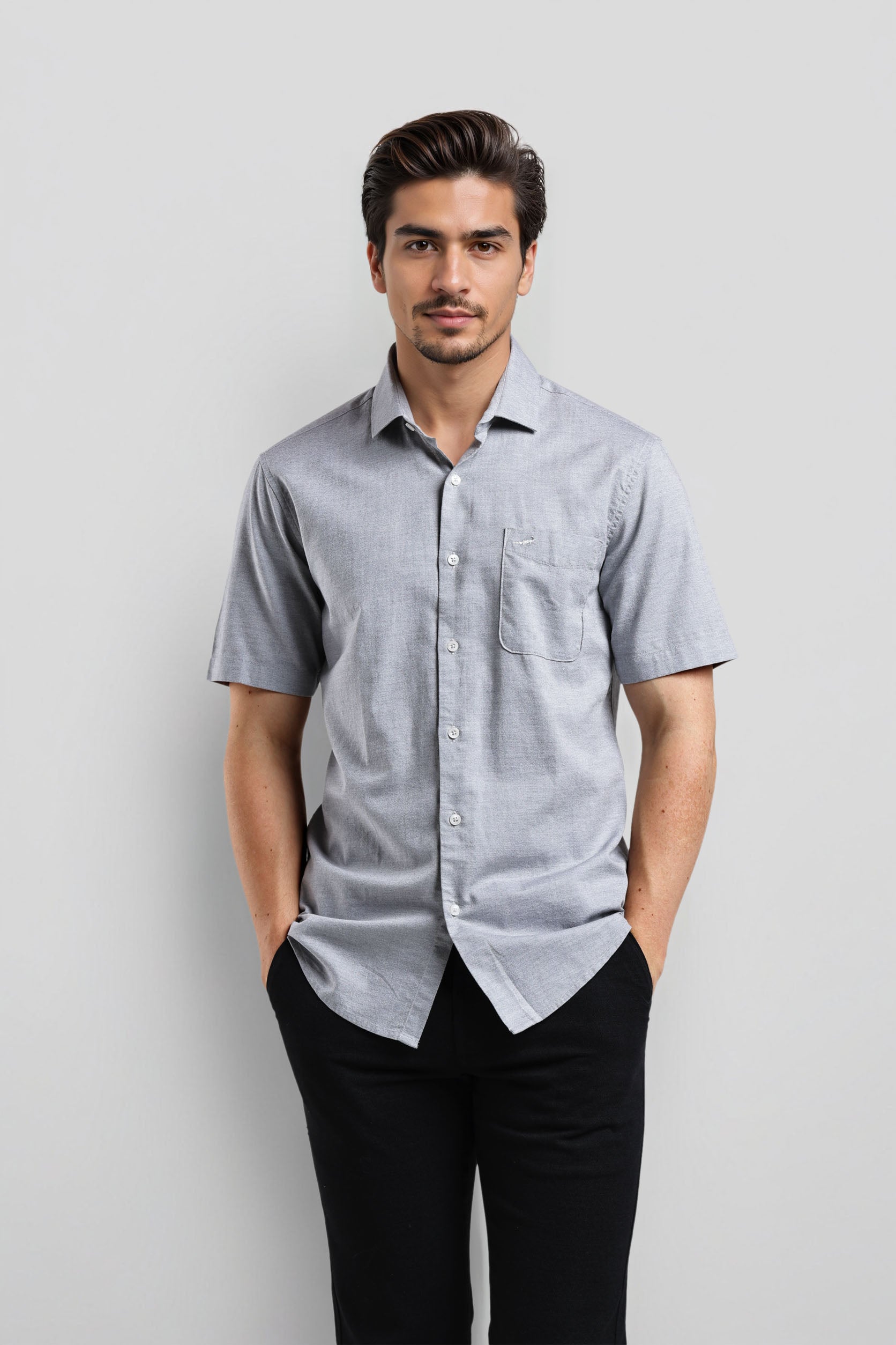 Man wearing a light blue checkered shirt and black pants against a gray background