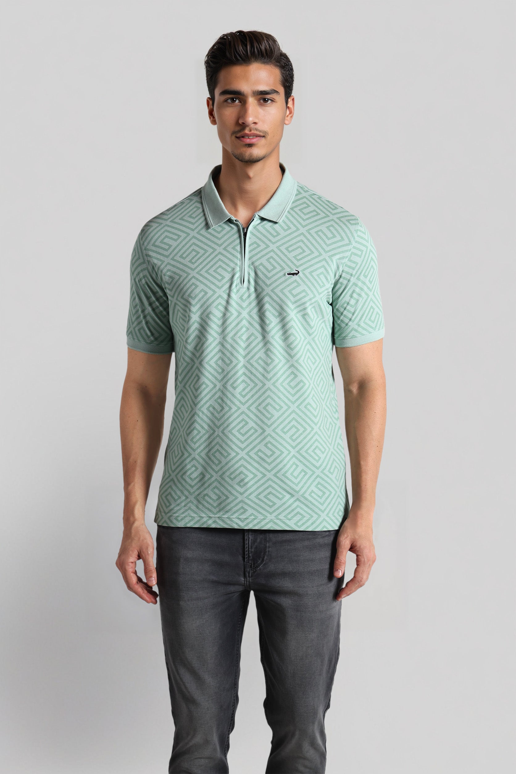 Man wearing a light green patterned polo shirt and dark jeans on a gray background