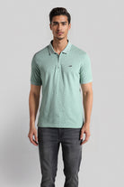 Man wearing a light green patterned polo shirt and dark jeans on a gray background