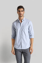 Man wearing a light blue button-up shirt with rolled-up sleeves and gray pants on a plain background