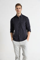 Man wearing a dark blue button-up shirt and light gray pants on a white background