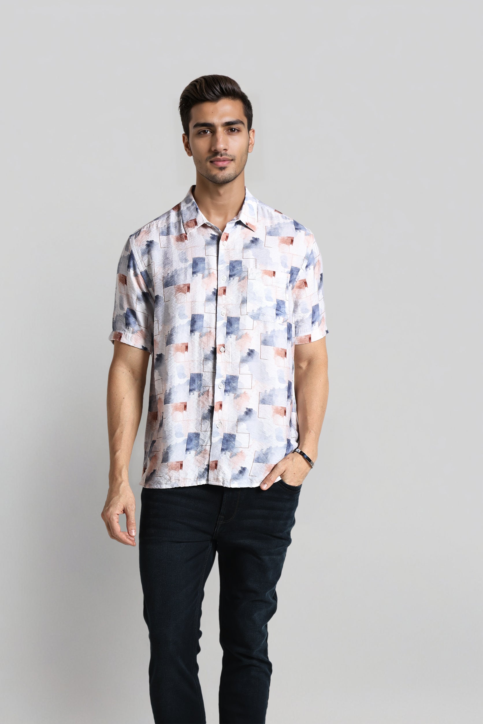 Man wearing a patterned shirt and dark pants on a plain background