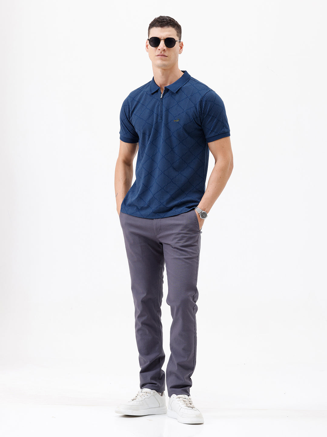 A man wearing a navy blue short-sleeve polo shirt with a subtle geometric pattern and a half-zip collar, paired with gray trousers, against a plain white background.