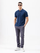 A man wearing a navy blue short-sleeve polo shirt with a subtle geometric pattern and a half-zip collar, paired with gray trousers, against a plain white background.