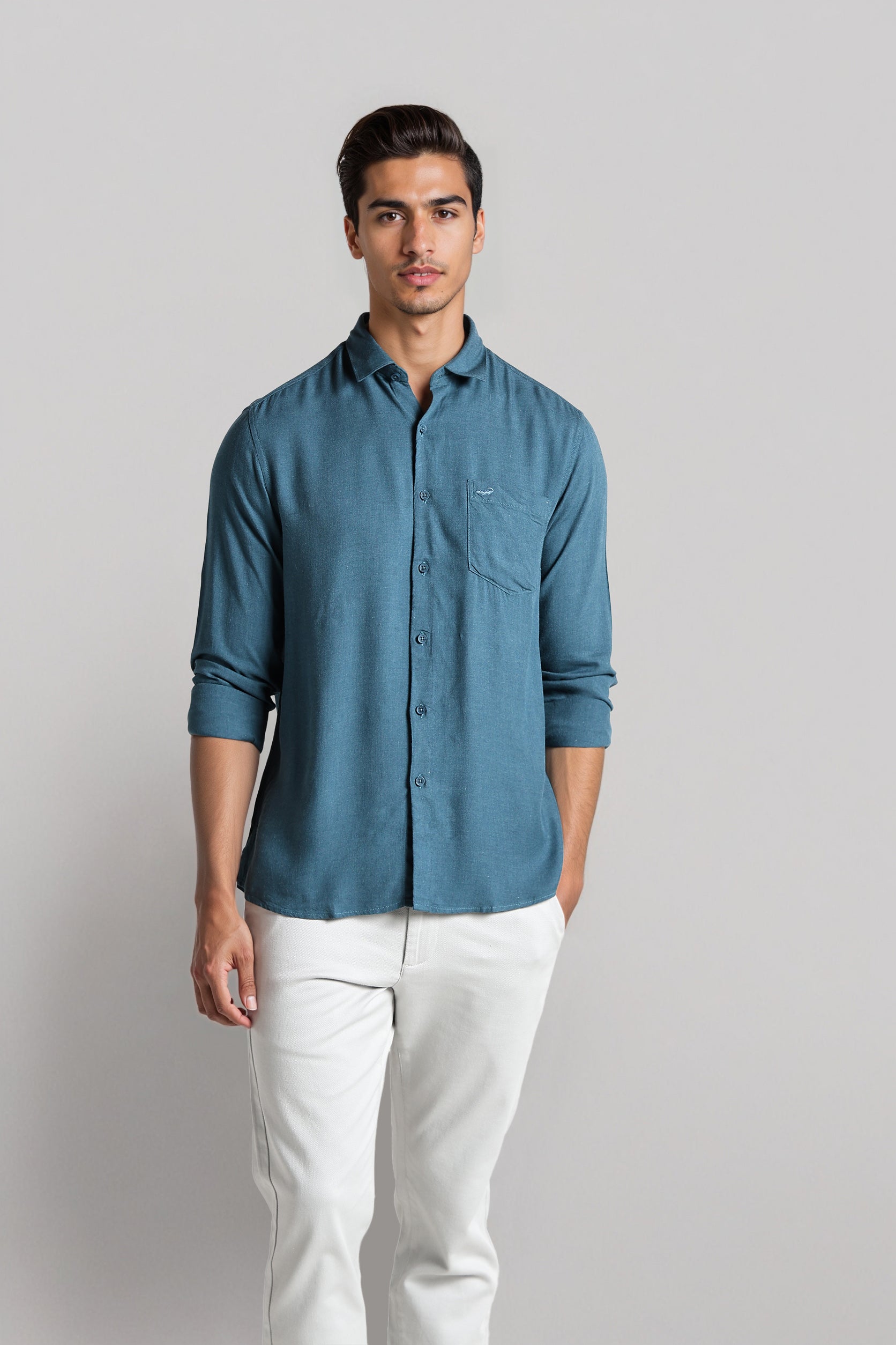 Man wearing a blue shirt and white pants against a plain background