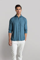 Man wearing a blue shirt and white pants against a plain background