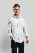 Man wearing a light blue shirt and dark pants on a plain background