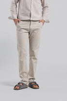 Person wearing a light-colored shirt and pants with sandals on a plain background