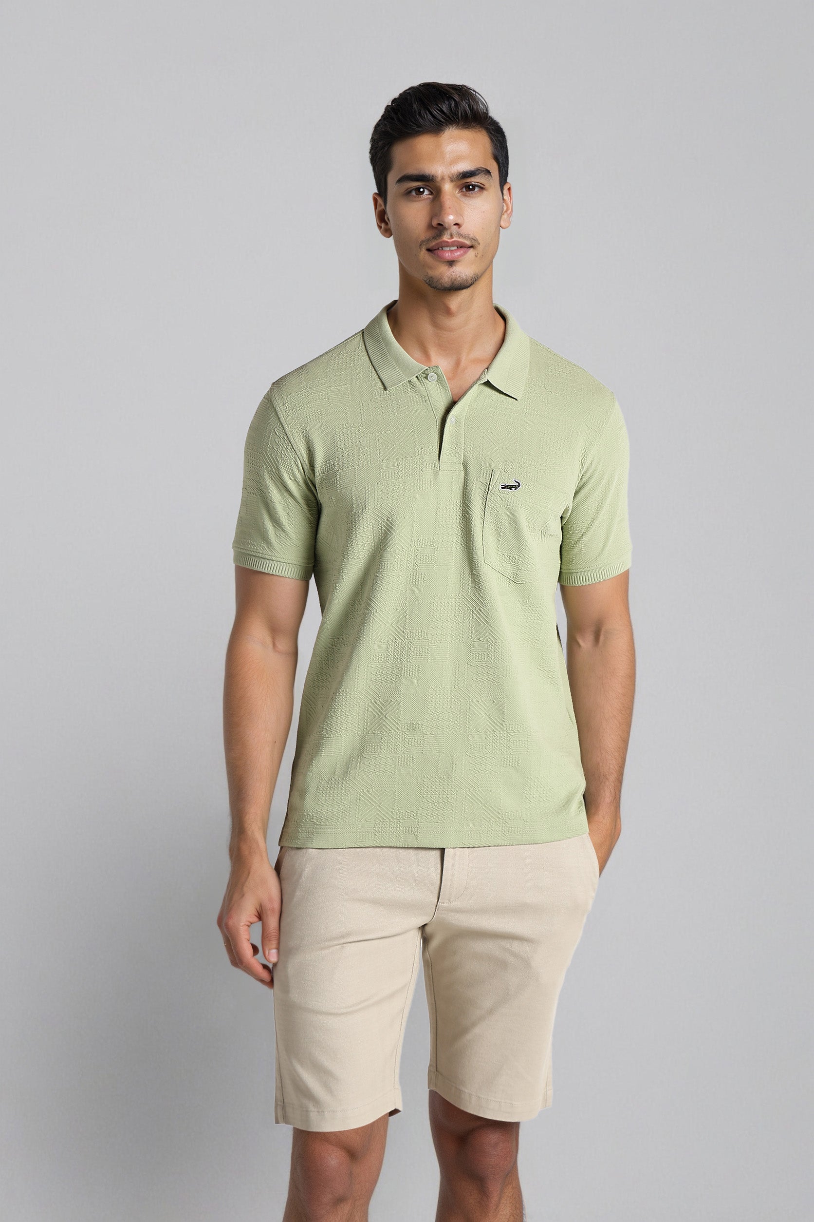 Man wearing a light green polo shirt and beige shorts on a gray background