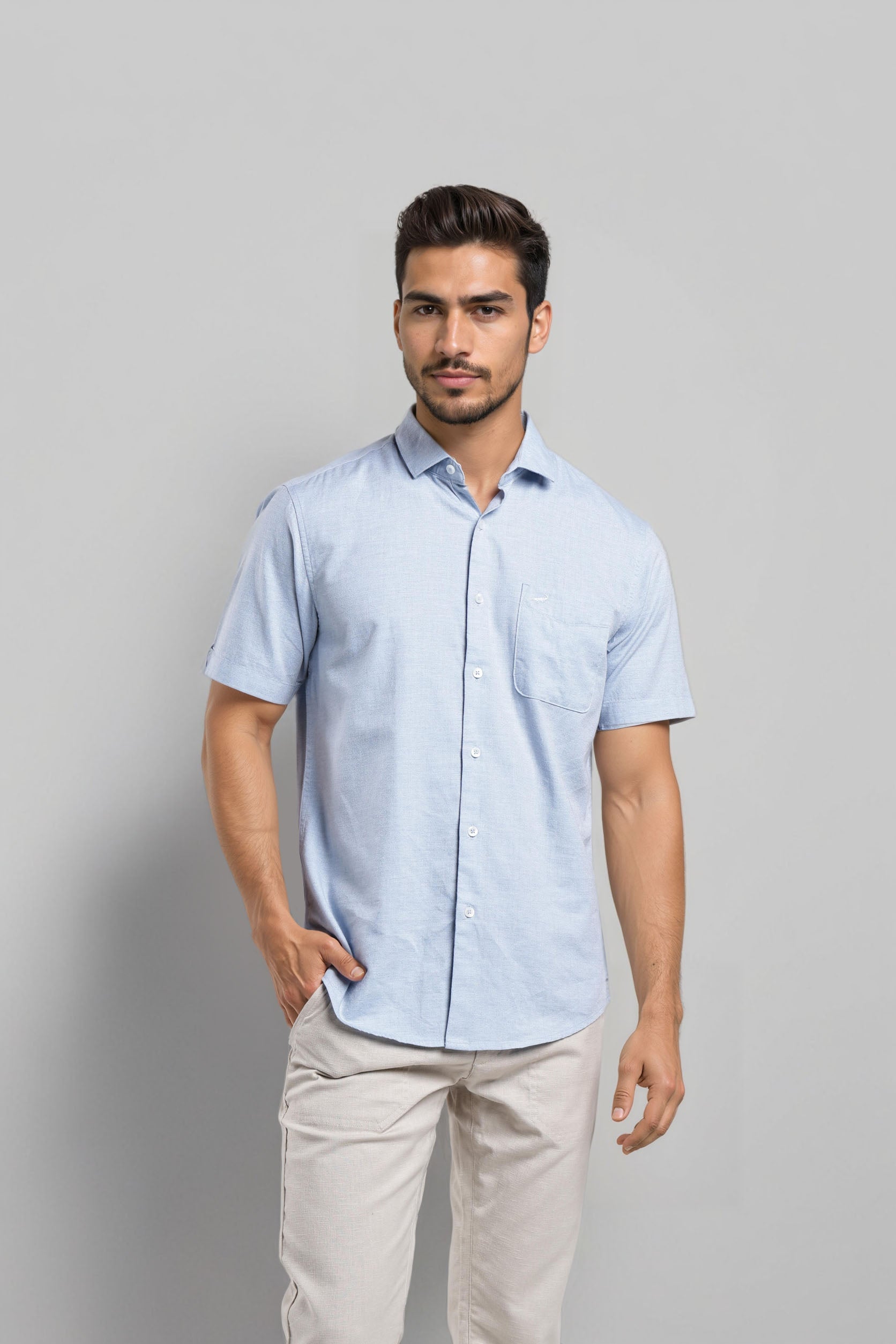 Man wearing a light blue checkered shirt and beige pants against a gray background