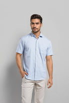 Man wearing a light blue checkered shirt and beige pants against a gray background