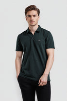 Man wearing a dark green polo shirt on a light gray background