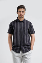 Man wearing a dark patterned shirt and light pants on a white background