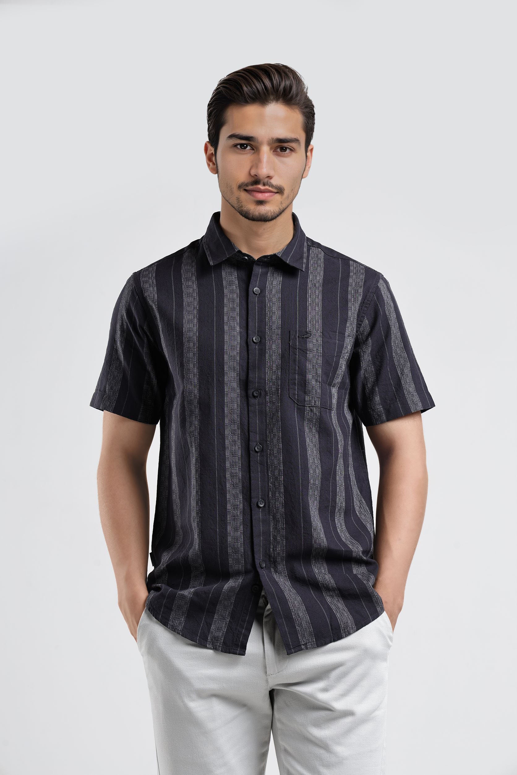 Man wearing a dark patterned shirt and light pants on a white background