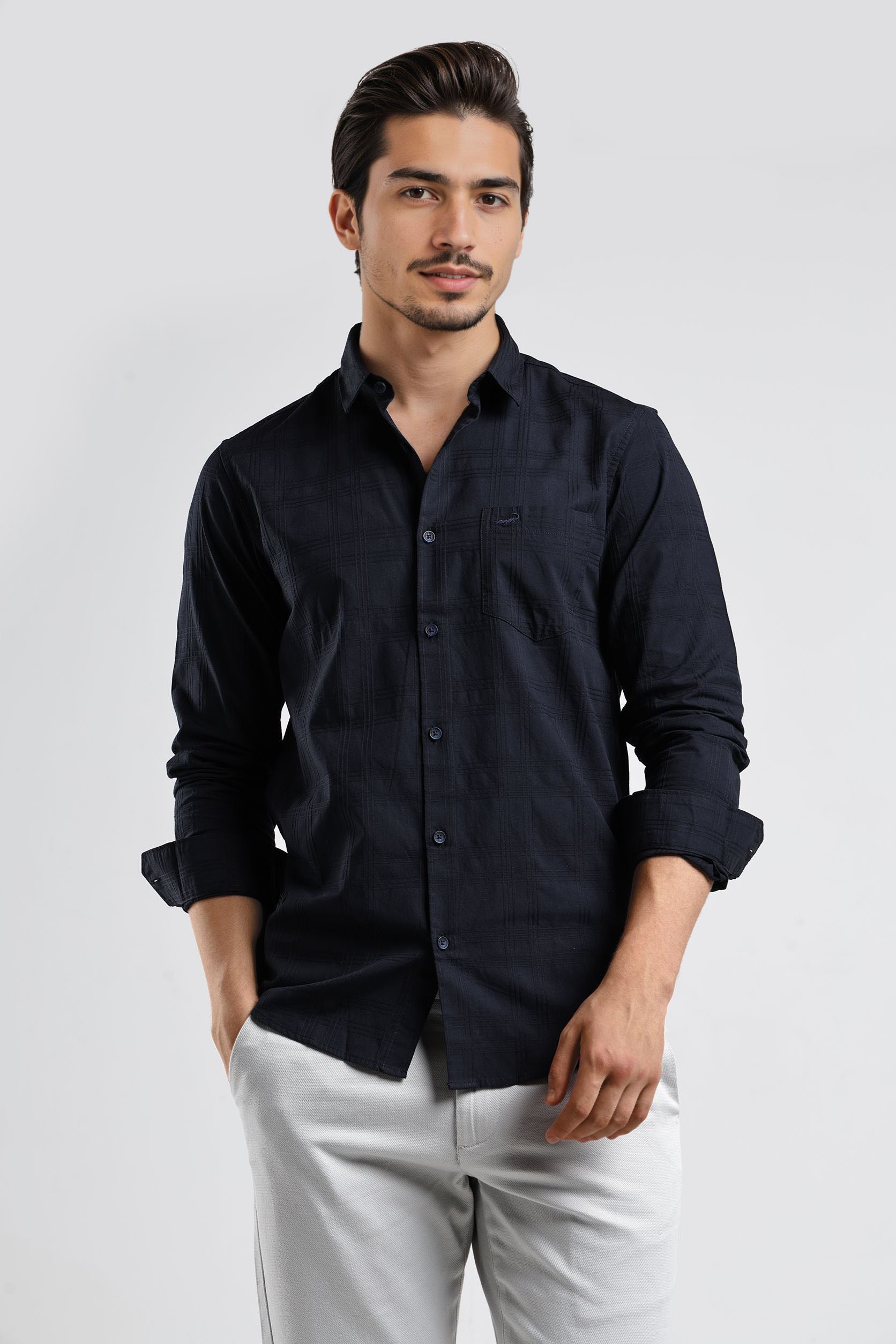 Man wearing a black button-up shirt and white pants on a light gray background