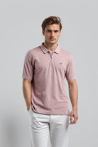 Man wearing a pink patterned polo shirt and white pants against a gray background