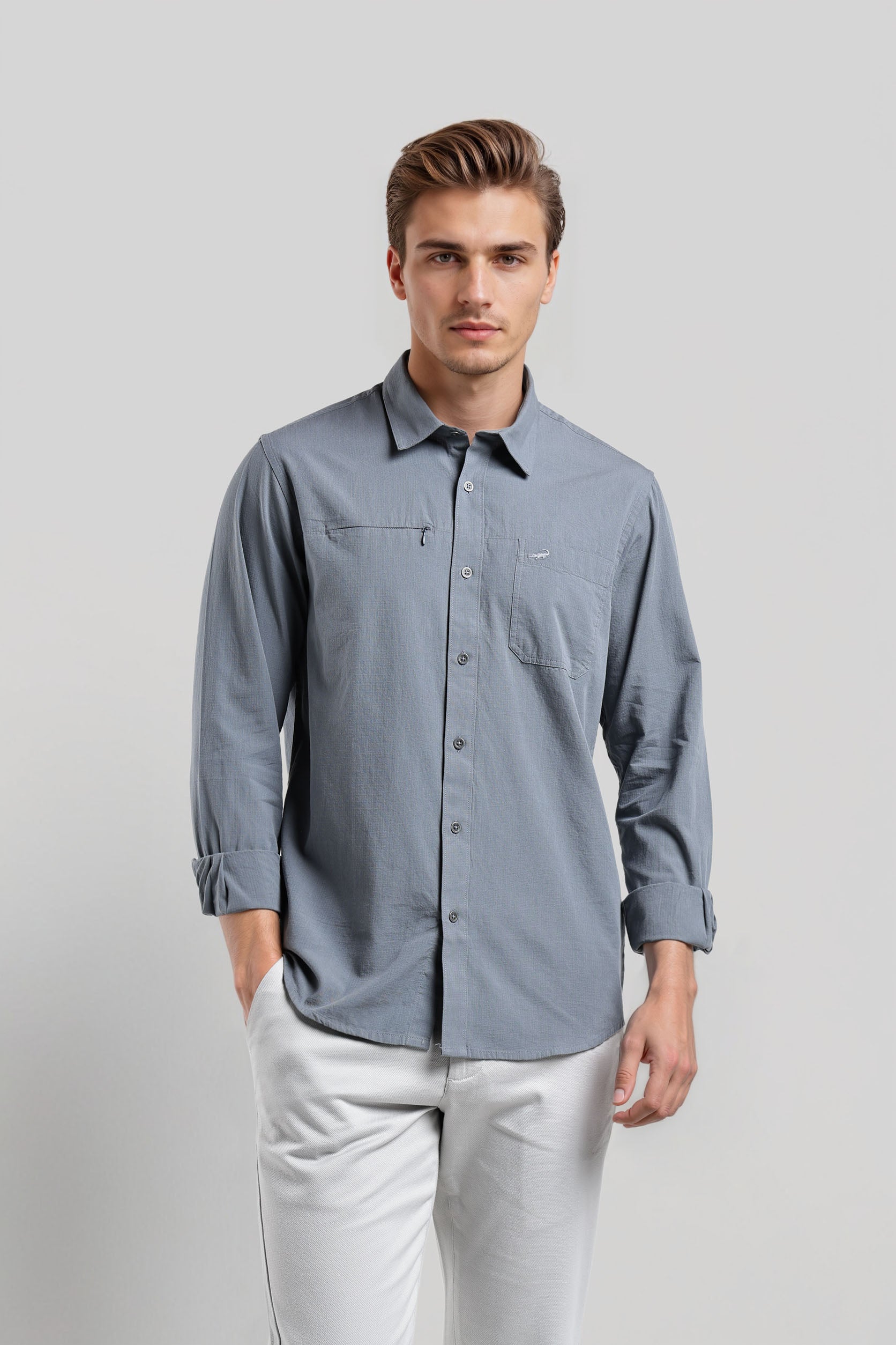 Man wearing a light blue button-up shirt and white pants on a gray background