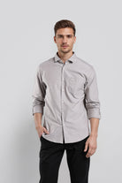 Man wearing a light gray button-up shirt and black pants against a white background