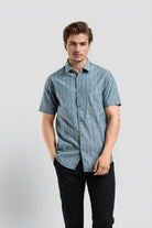 Man wearing a blue checkered shirt and black pants on a light gray background