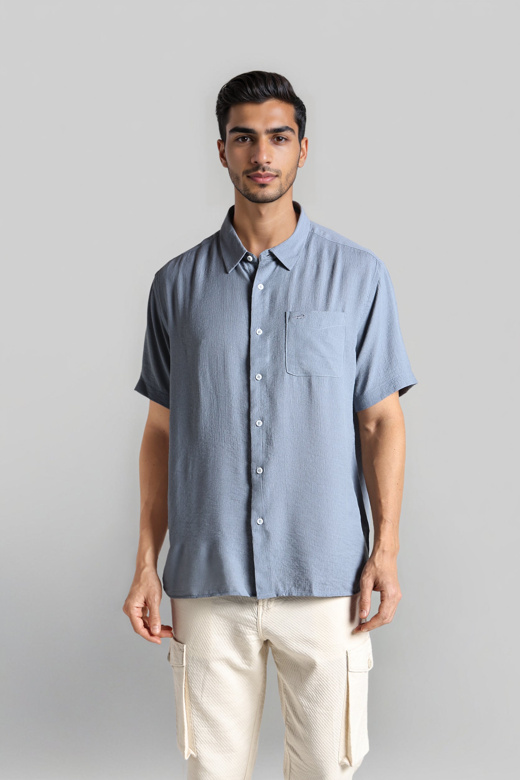 Man wearing a light blue short-sleeve shirt and beige pants against a gray background