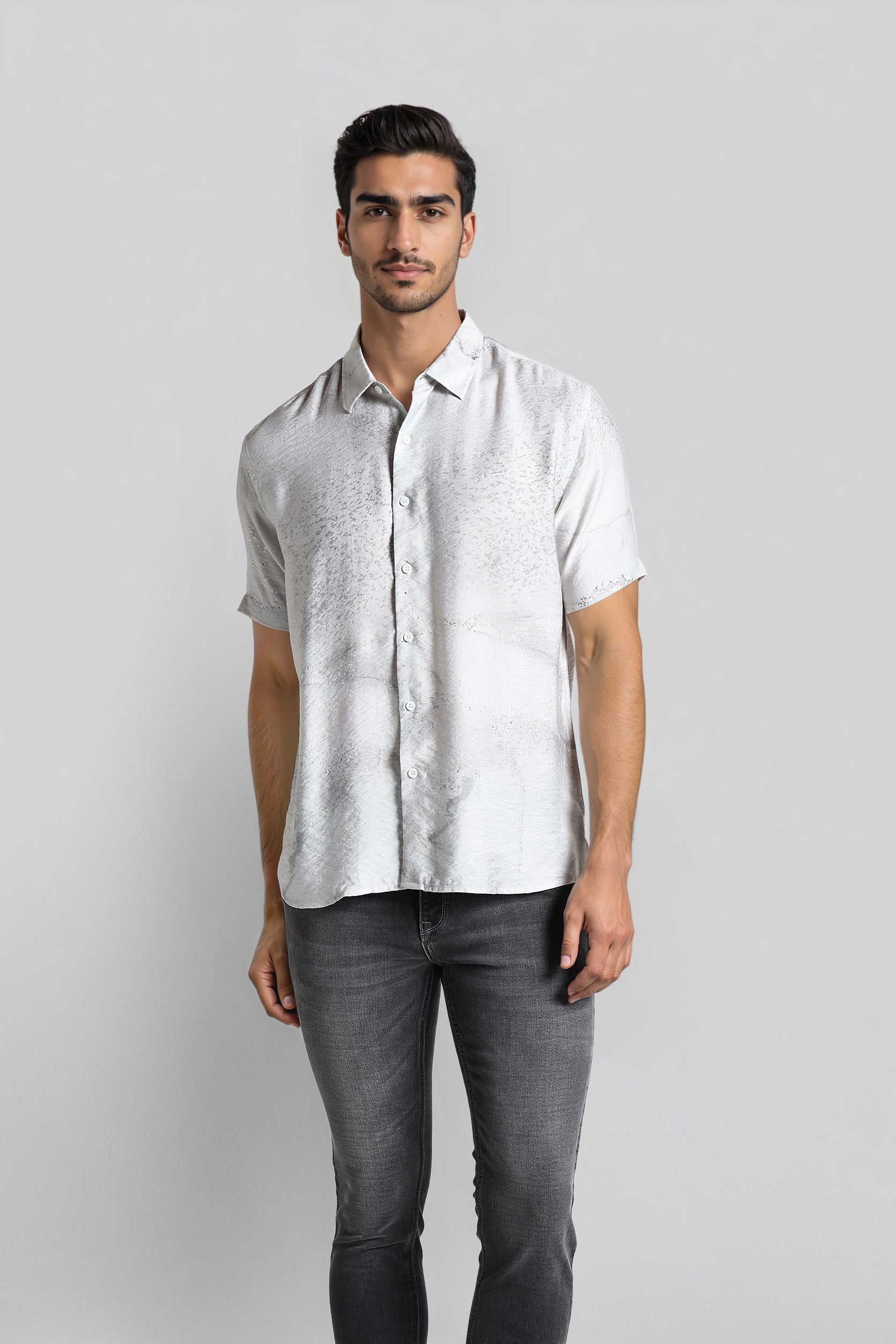 Man wearing a light gray patterned shirt and dark gray jeans on a white background