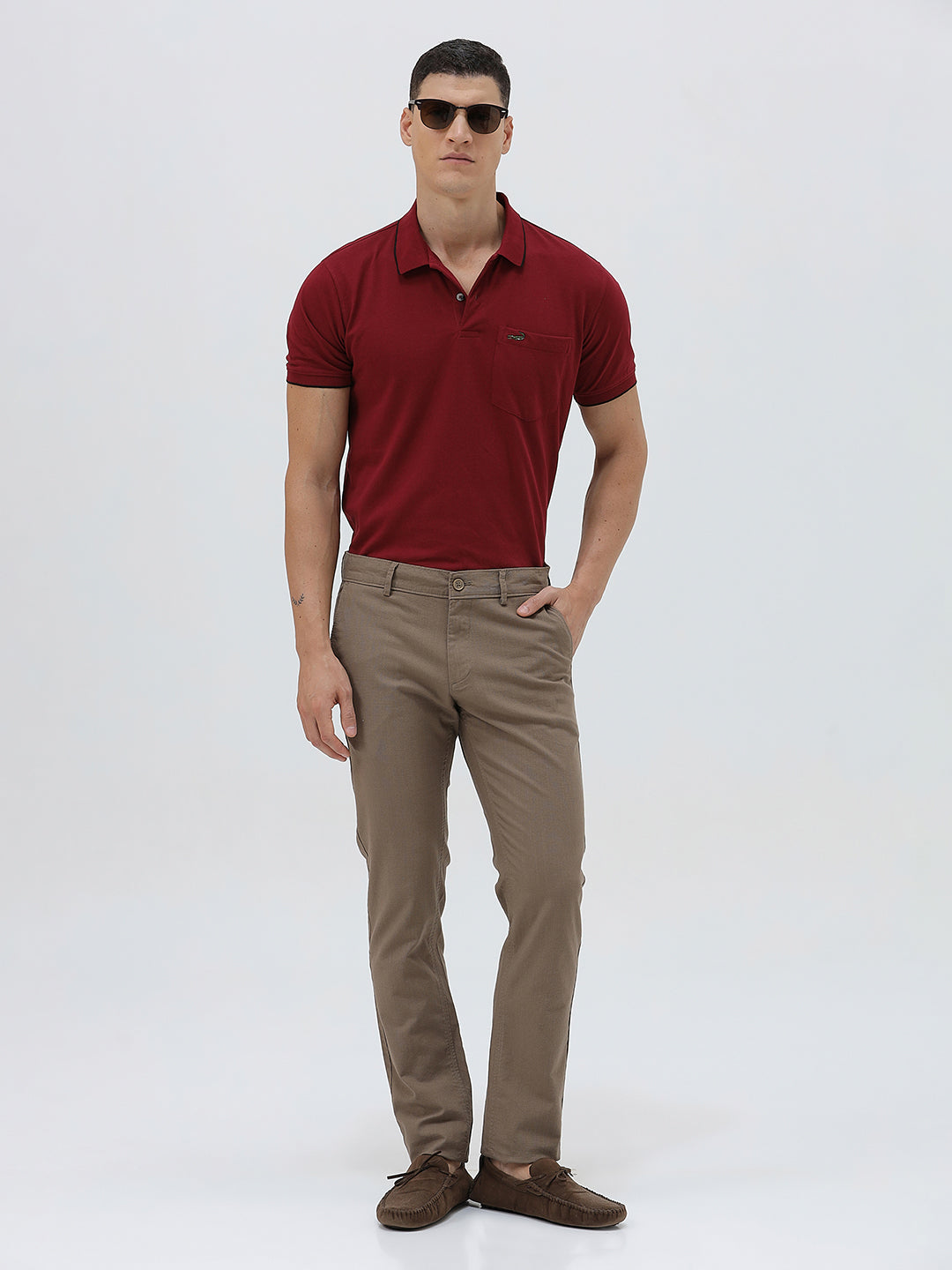 A person wearing slim-fit brown trousers, paired with a dark red shirt and brown suede moccasin shoes, shown from the waist down against a plain white studio background.