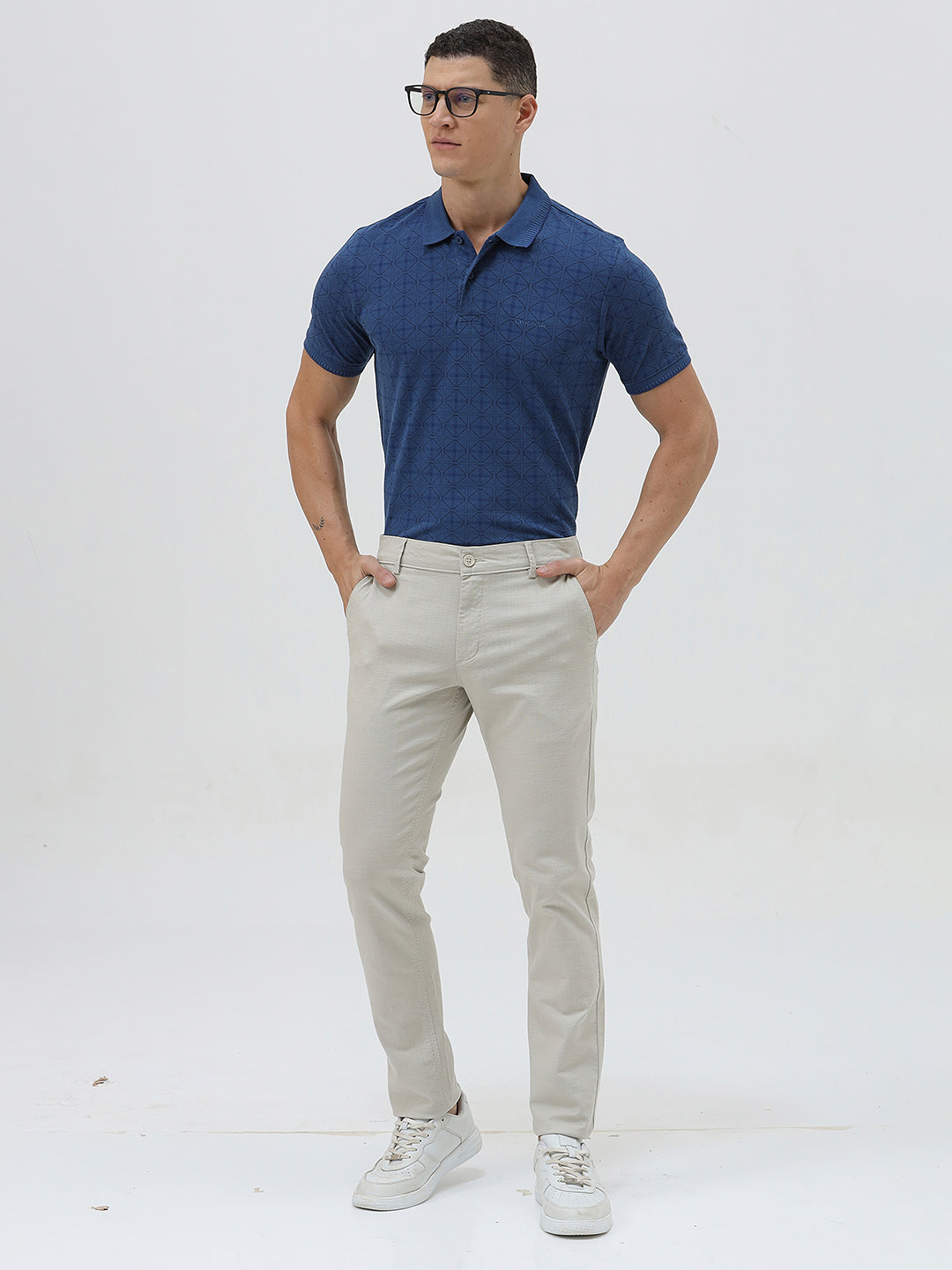 A person wearing light beige slim-fit chino pants, a navy blue t-shirt, and white sneakers, standing against a plain white studio background.