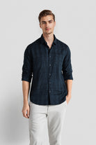 Man wearing a dark blue button-up shirt and light gray pants on a white background