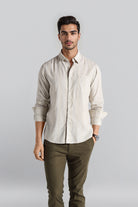 Man wearing a beige shirt and green pants against a plain background