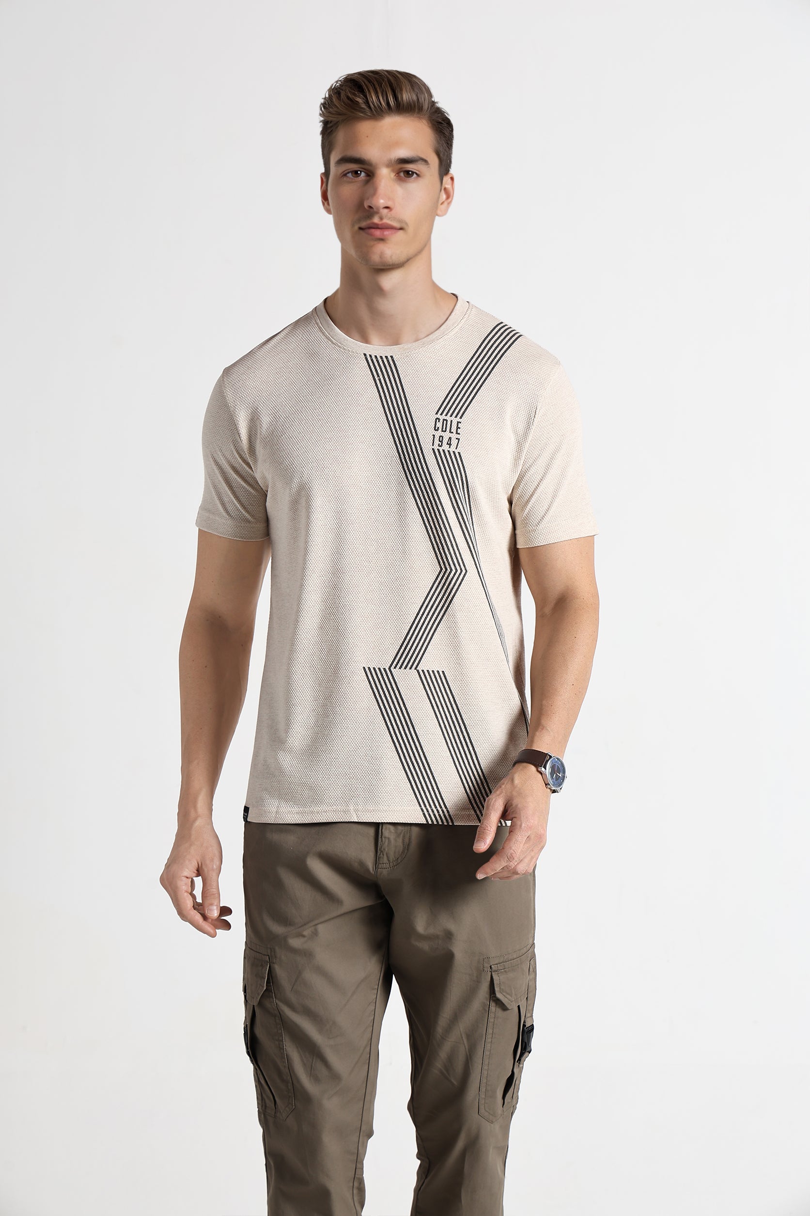 Man wearing a beige t-shirt with a geometric design and brown cargo pants on a white background