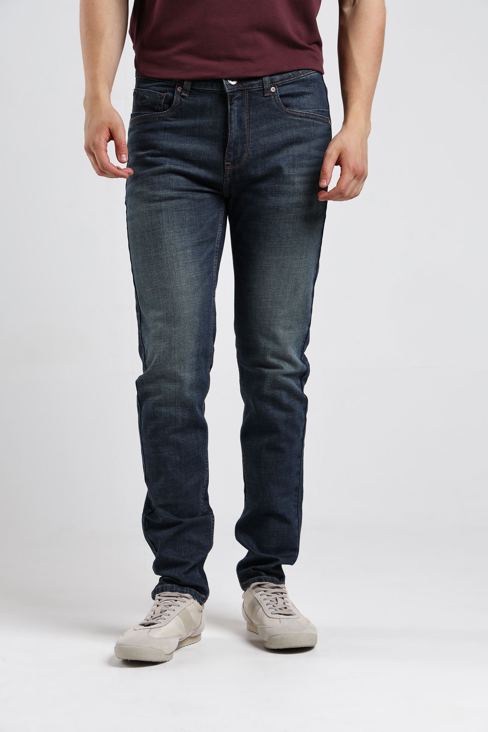 Person wearing dark blue jeans and a maroon shirt on a white background