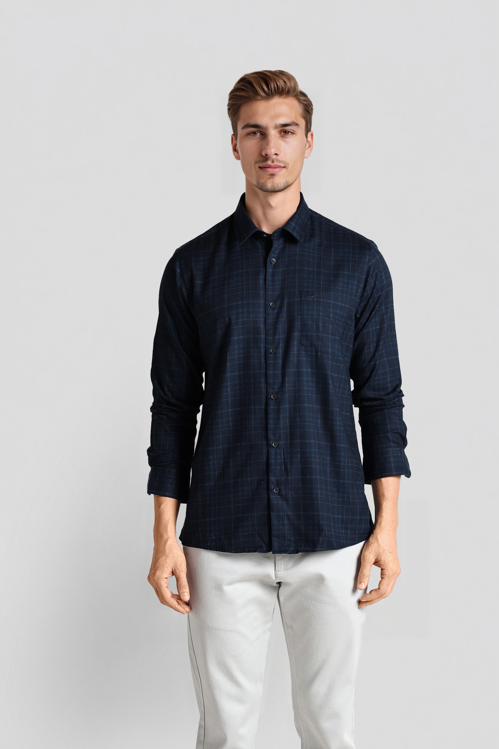 Man wearing a dark blue checkered shirt and white pants on a light gray background