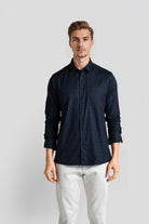 Man wearing a dark blue checkered shirt and white pants on a light gray background