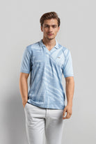 Man wearing a light blue patterned polo shirt and light gray pants on a gray background