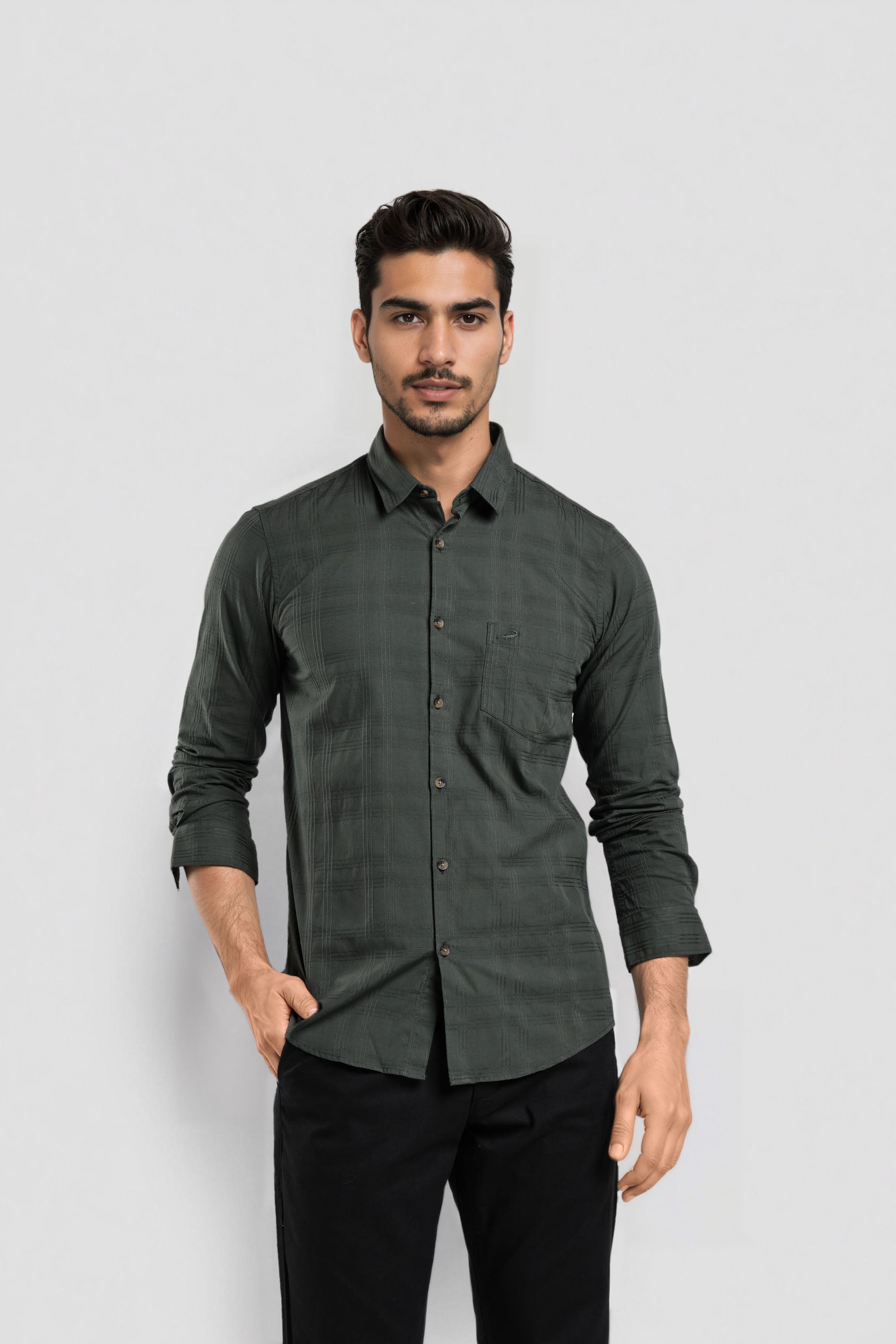 Man wearing a dark green button-up shirt and black pants on a light gray background