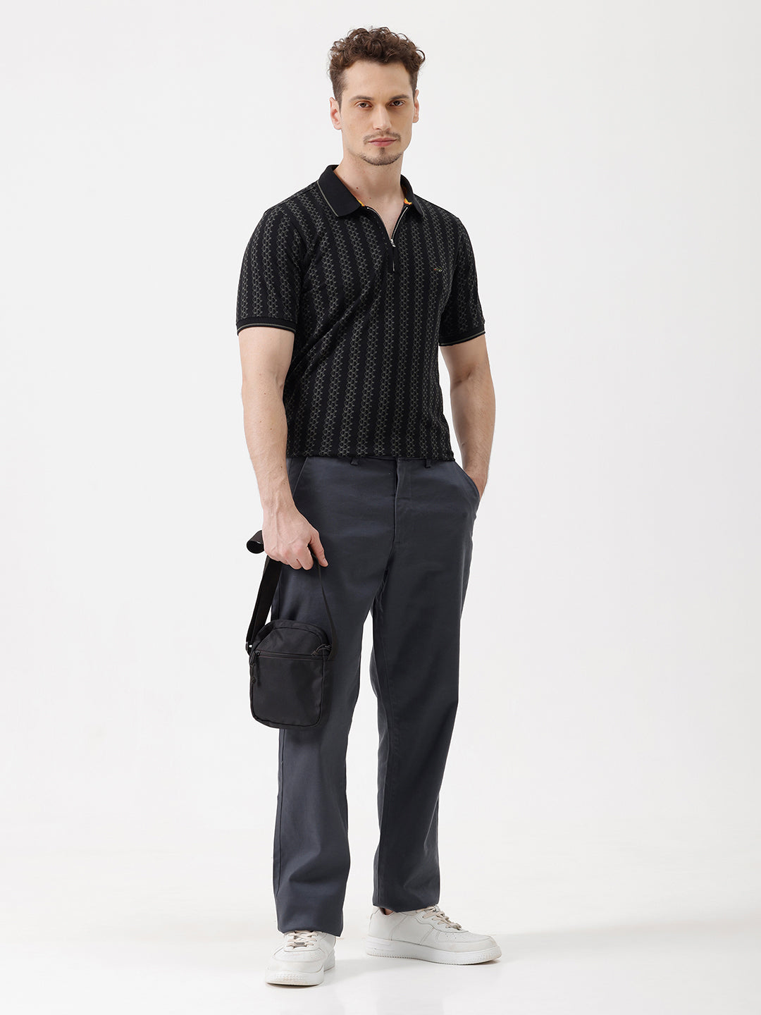 A man wearing a black short-sleeve polo shirt with a subtle geometric pattern, paired with dark gray trousers, standing against a plain white studio background.