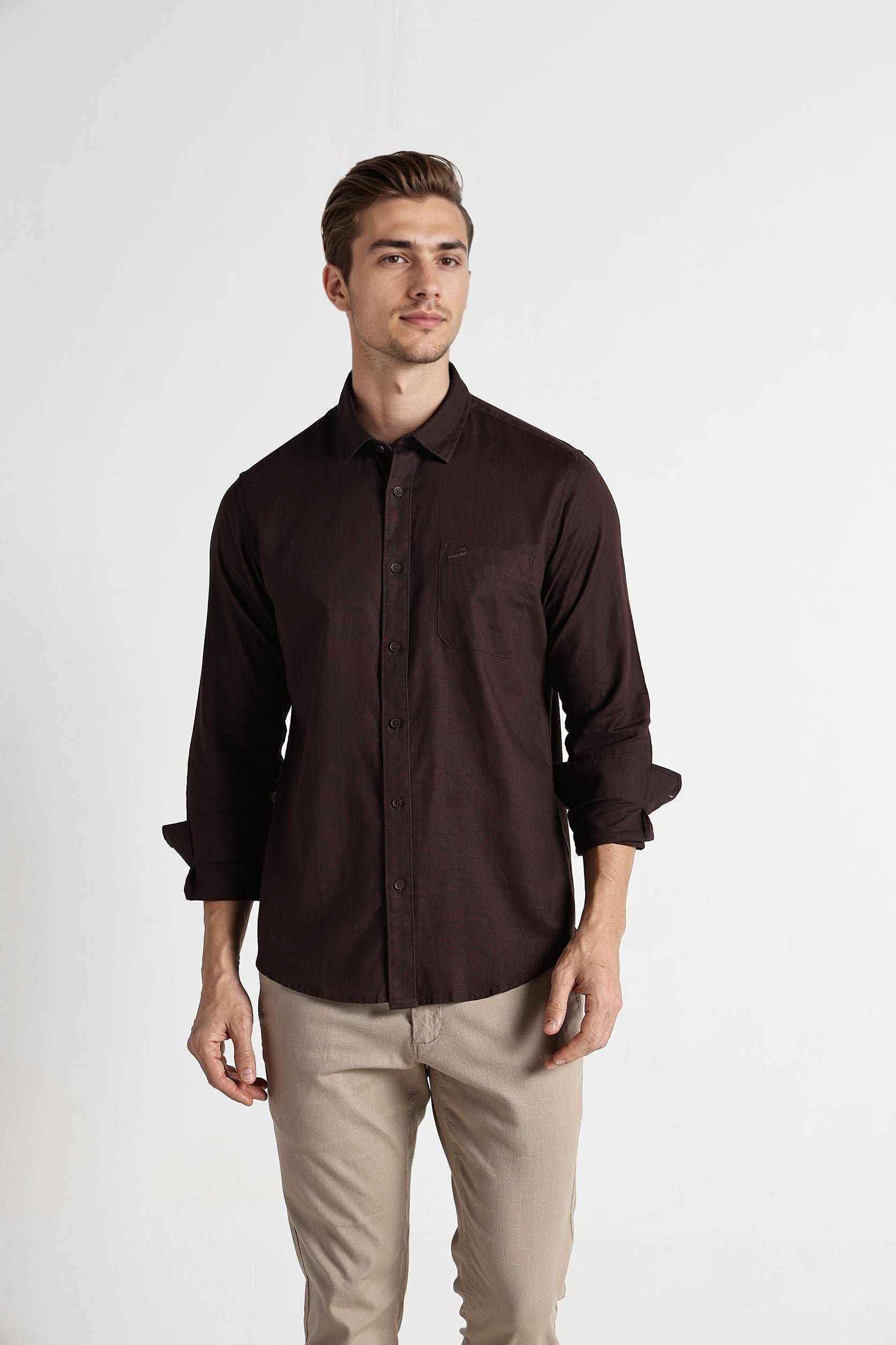 Man wearing a dark brown button-up shirt and beige pants on a white background