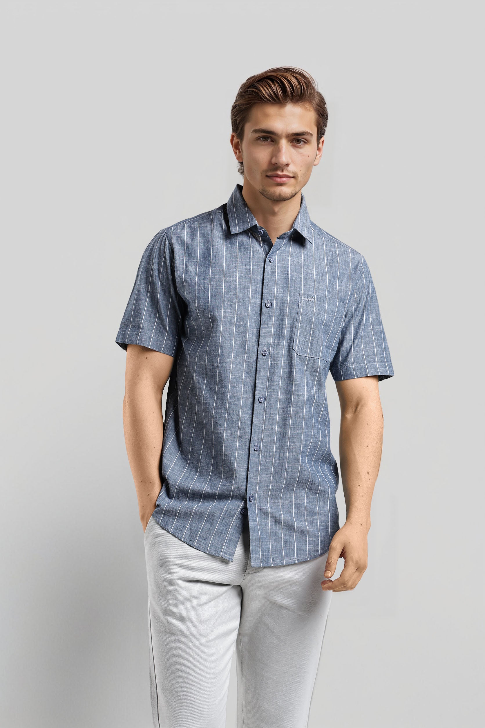 Man wearing a blue checkered shirt and light gray pants against a plain background