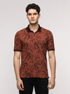 Man wearing a brown abstract tropical leaf printed polo t shirt in brown on a light gray background