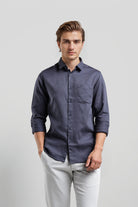 Man wearing a dark blue button-up shirt and light gray pants on a plain background