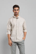 Man wearing a beige shirt and gray pants against a gray background