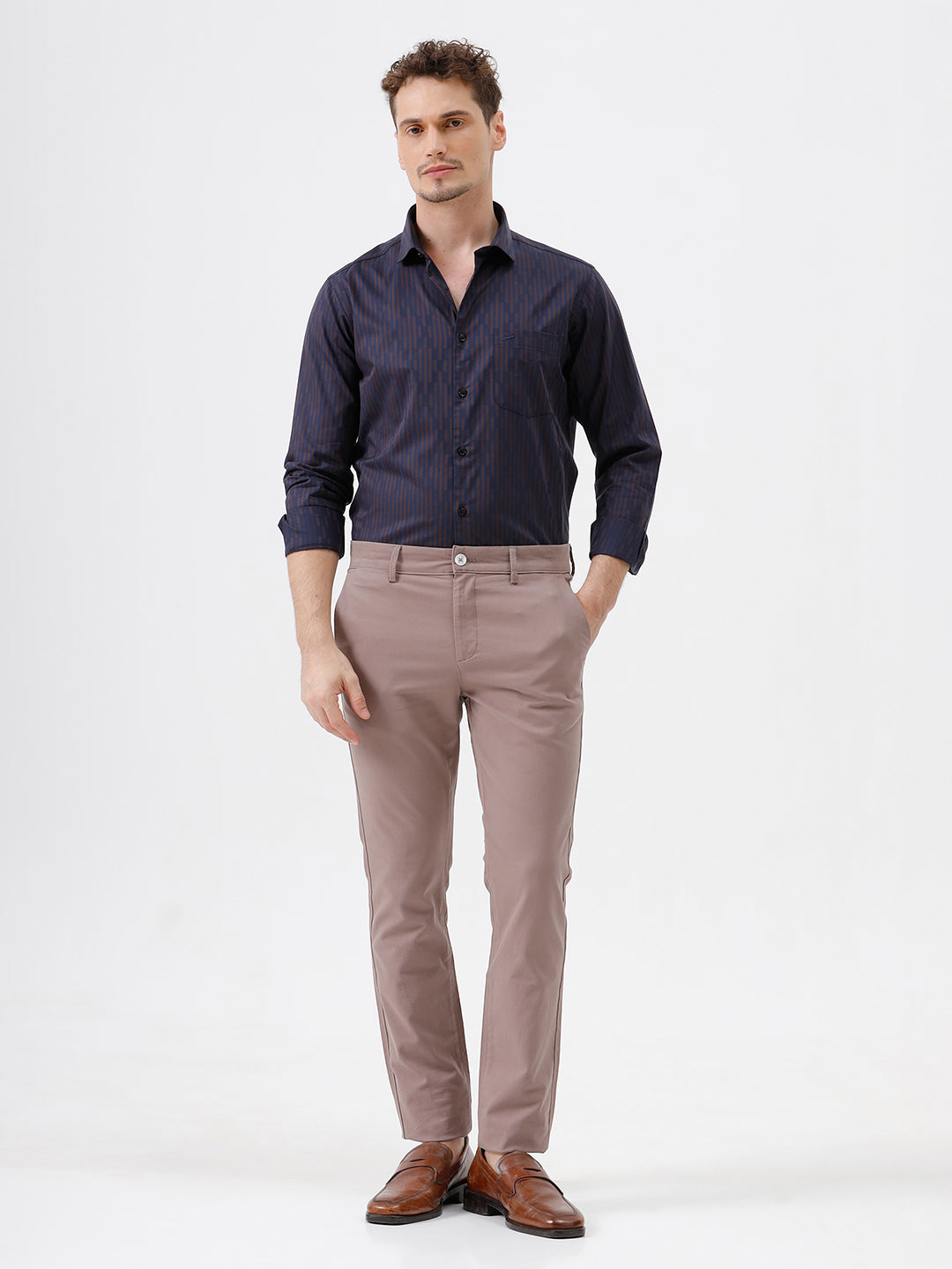 A man wearing a dark navy blue button-down shirt with thin vertical red stripes and light brown trousers, standing against a plain white studio background.