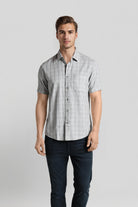 Man wearing a checkered short-sleeve shirt and dark pants on a light gray background