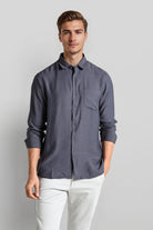 Man wearing a dark gray button-up shirt and light-colored pants on a plain background