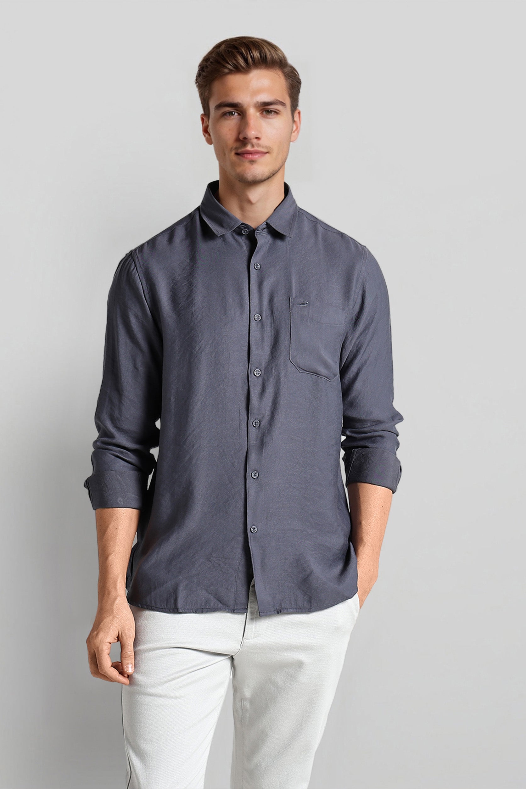 Man wearing a dark gray button-up shirt and light-colored pants on a plain background