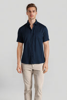 Man wearing a navy short-sleeve shirt and beige pants on a light gray background