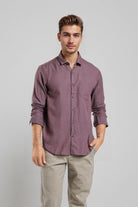 Man wearing a purple button-up shirt and beige pants against a gray background