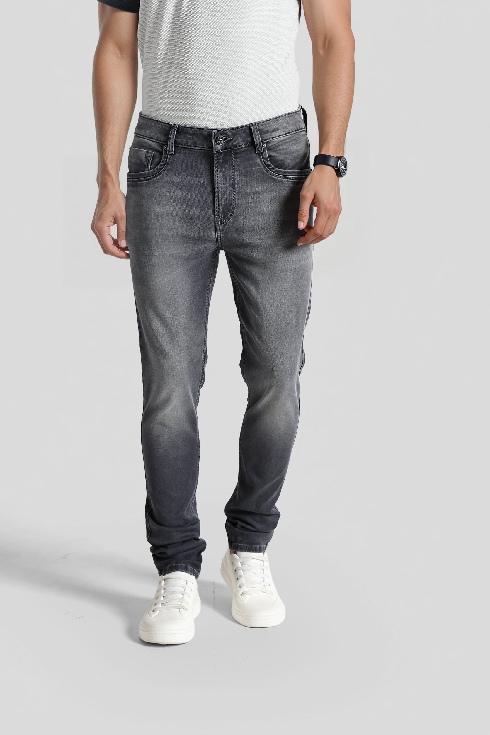 Person wearing gray jeans and white sneakers on a plain background