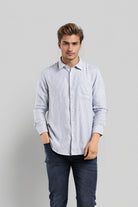 Man wearing a light blue striped shirt and dark jeans on a gray background