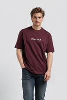 Man wearing a maroon t-shirt with a logo on a light gray background